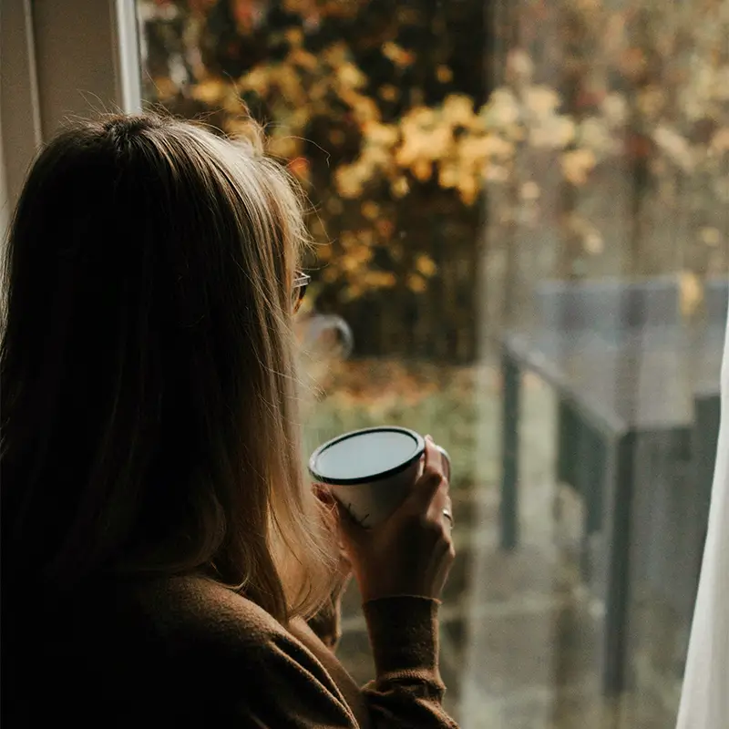 Kvinde med en kop kaffe ser ud ad vinduet